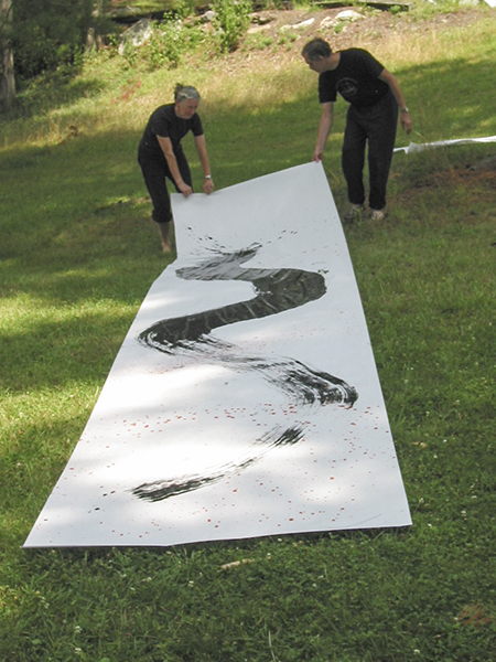 Long shot photograph of black calligraphy stroke painted by Philip Foster using a big brush on white paper outside on the grass
