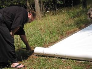 Bob Wing rolling out white paper on the grass in preparation for making his big brush stroke.