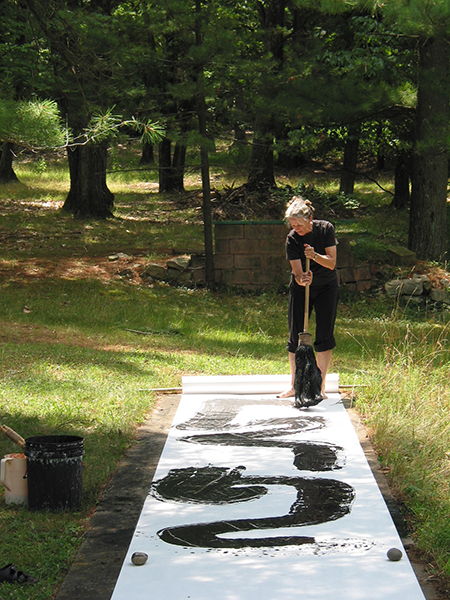 Long shot photograph of black calligraphy stroke painted by workshop participant using a big brush on white paper outside on the grass